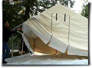 A man setting up a canvas wall tent.