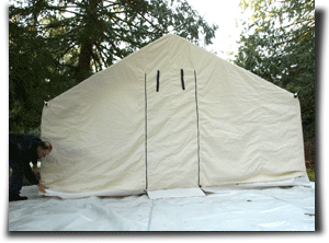 A man setting up a canvas wall tent.